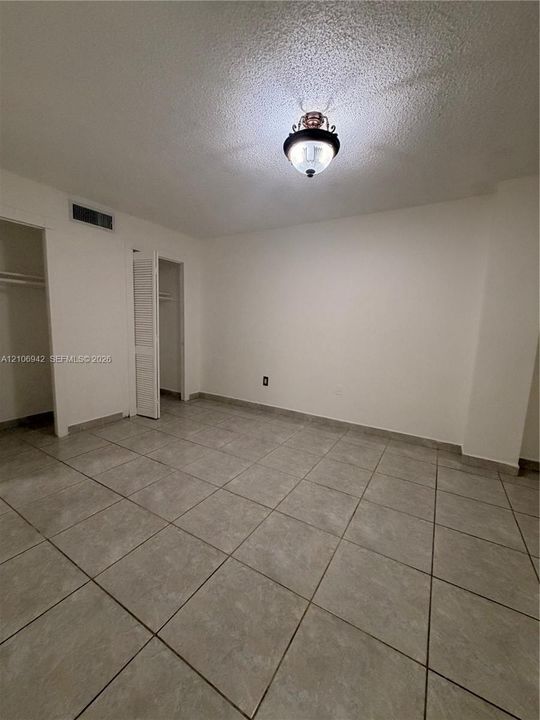 Interior room featuring large-format ceramic tile flooring, neutral wall finishes, a semi-flush mount light fixture, and two closets with louvered doors
