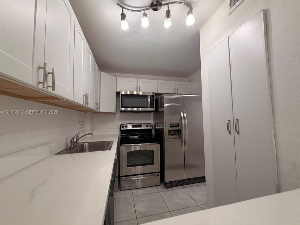Kitchen featuring white shaker-style cabinetry, solid-surface countertops, stainless steel appliances, tile flooring, and multi-bulb track lighting