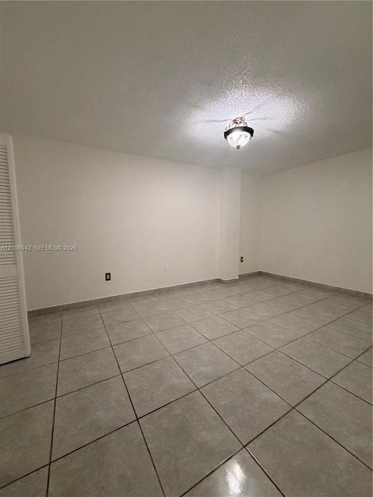 Neutral-tone tile flooring, white wall finishes, and louvered-style closet doors with a ceiling-mounted light fixture
