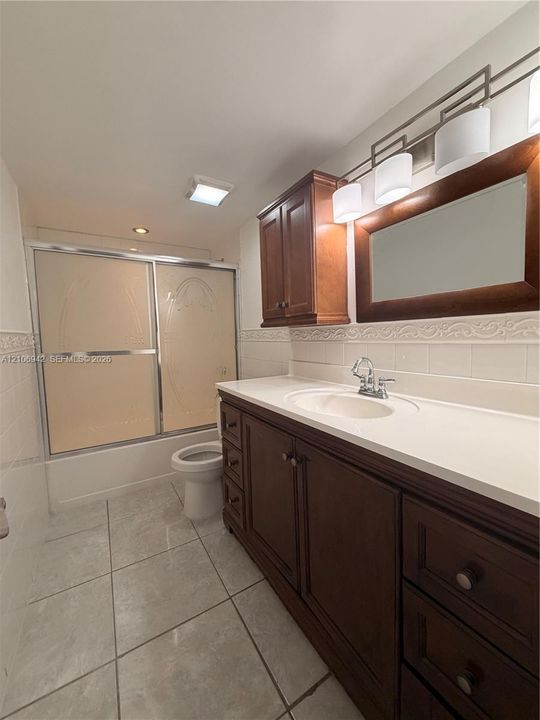 Bathroom featuring a vanity with wood-finish cabinetry, a white countertop with an integrated basin, a coordinating wood-framed mirror, a multi-light fixture, and a sliding glass shower door