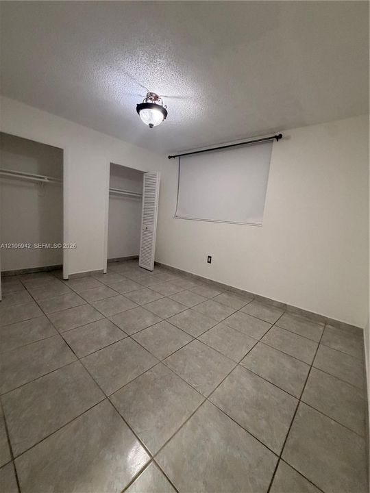 Neutral-toned ceramic tile flooring, two closets featuring white louvered doors, and a ceiling-mounted light fixture