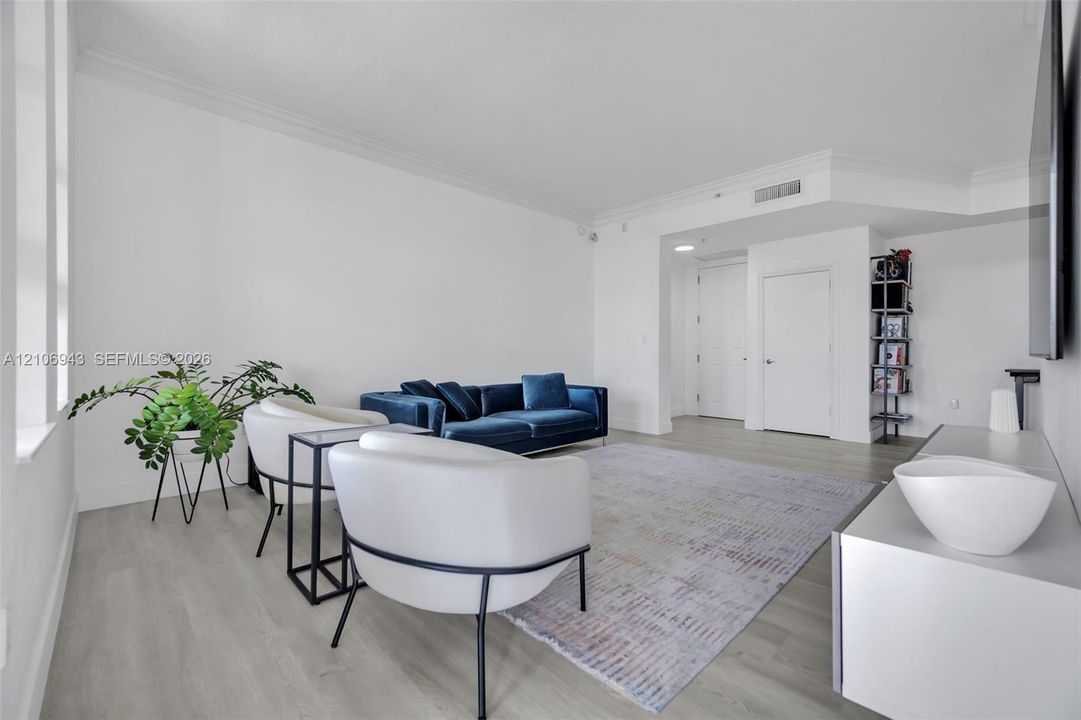 Open-concept living space featuring wood-finish flooring, crisp neutral wall paint, crown molding, and tall vertical windows