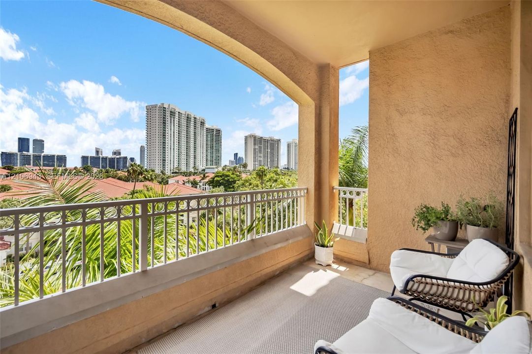 Covered balcony featuring stucco walls, stone flooring, and a metal railing