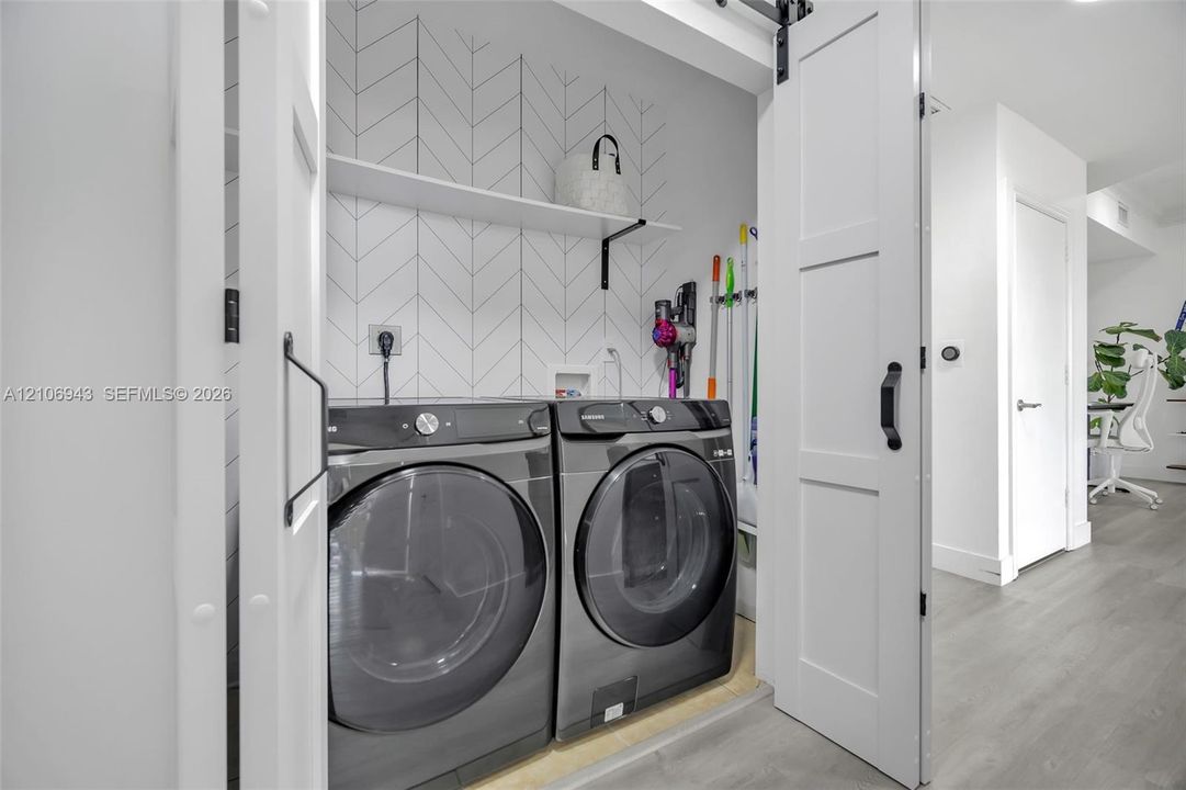 Laundry area featuring a sliding barn door, herringbone-patterned tile backsplash, and built-in shelving