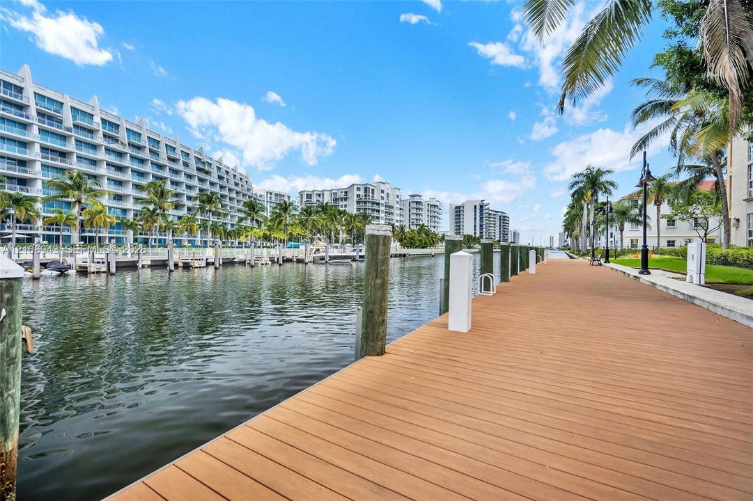 Waterfront boardwalk featuring a wood-finish deck, vertical wood pilings, and lamp post lighting