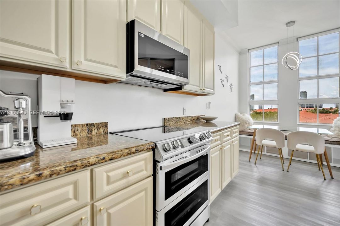 Kitchen featuring cream-colored cabinetry, stone countertops, stainless steel dual-oven range, built-in microwave, and large grid-pane windows