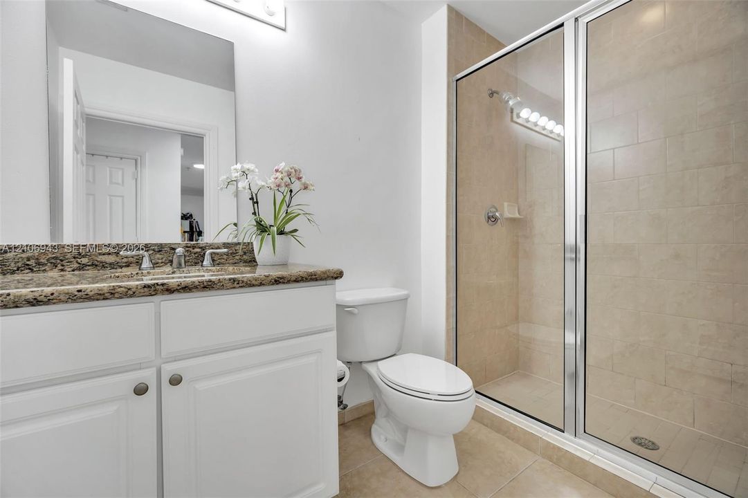 Bathroom featuring a vanity with white cabinetry, a stone-finish countertop, an integrated sink with a chrome faucet, a walk-in shower with glass enclosure, and tiled flooring
