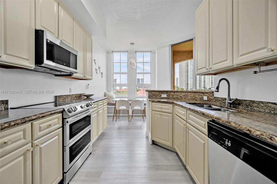 Kitchen featuring off-white cabinetry, stone countertops, stainless steel appliances, and large dual-pane windows