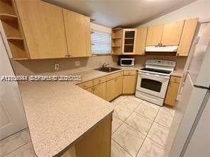 Kitchen featuring natural wood-finish cabinetry, light-toned laminate countertops, ceramic tile flooring, and integrated built-in shelving