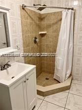 Bathroom featuring a white vanity cabinet, ceramic tile flooring, and a corner shower enclosure with neutral-toned wall tile, built-in shelving, and a chrome rainfall showerhead