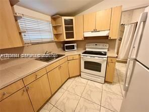 Kitchen featuring wood-finish cabinetry, neutral tile flooring, integrated range hood, stainless steel sink, and light-toned countertops