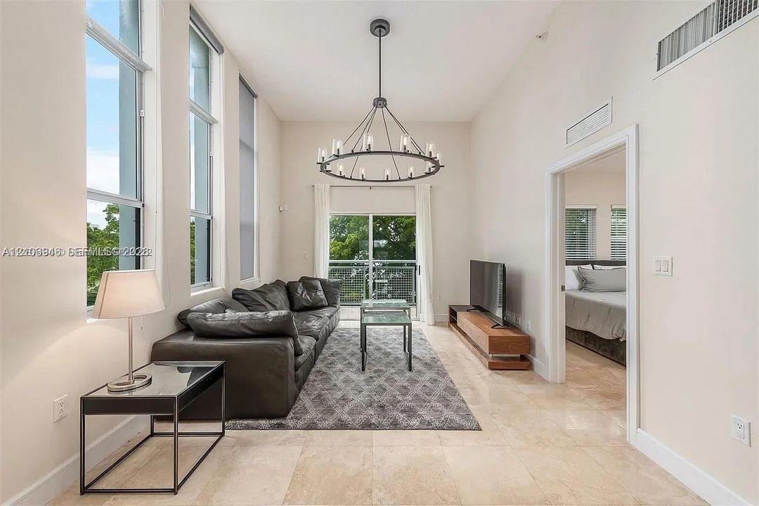 High ceilings with floor-to-ceiling windows, polished stone flooring, and a decorative circular chandelier