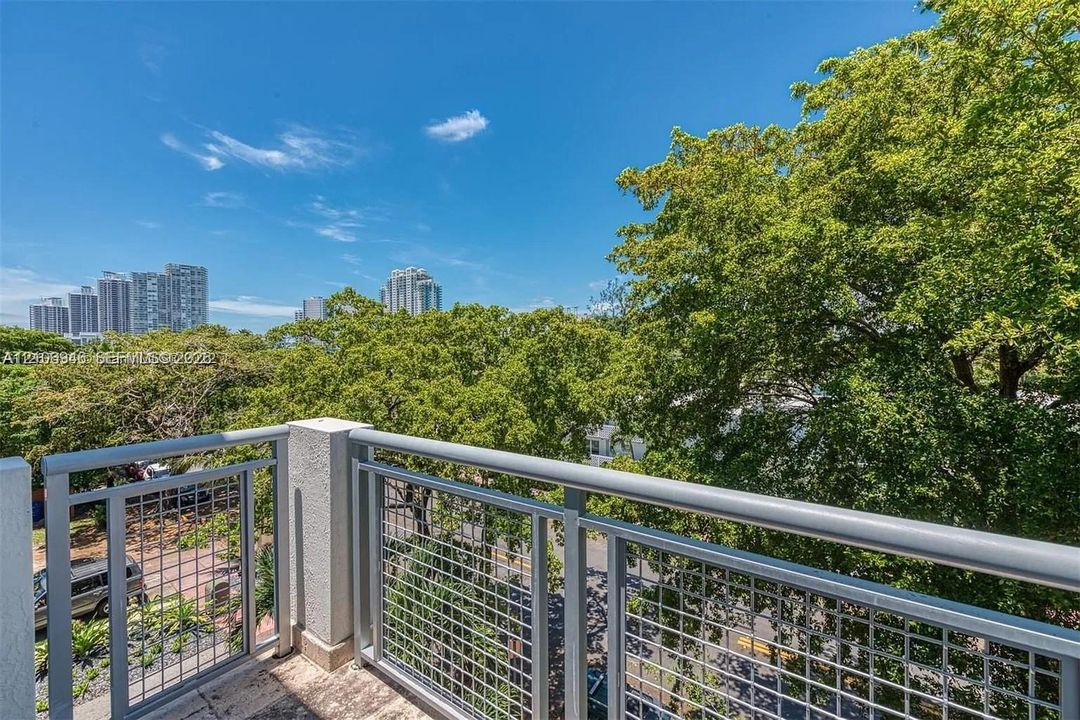 Private balcony with metal mesh railings, concrete flooring, and mature canopy trees