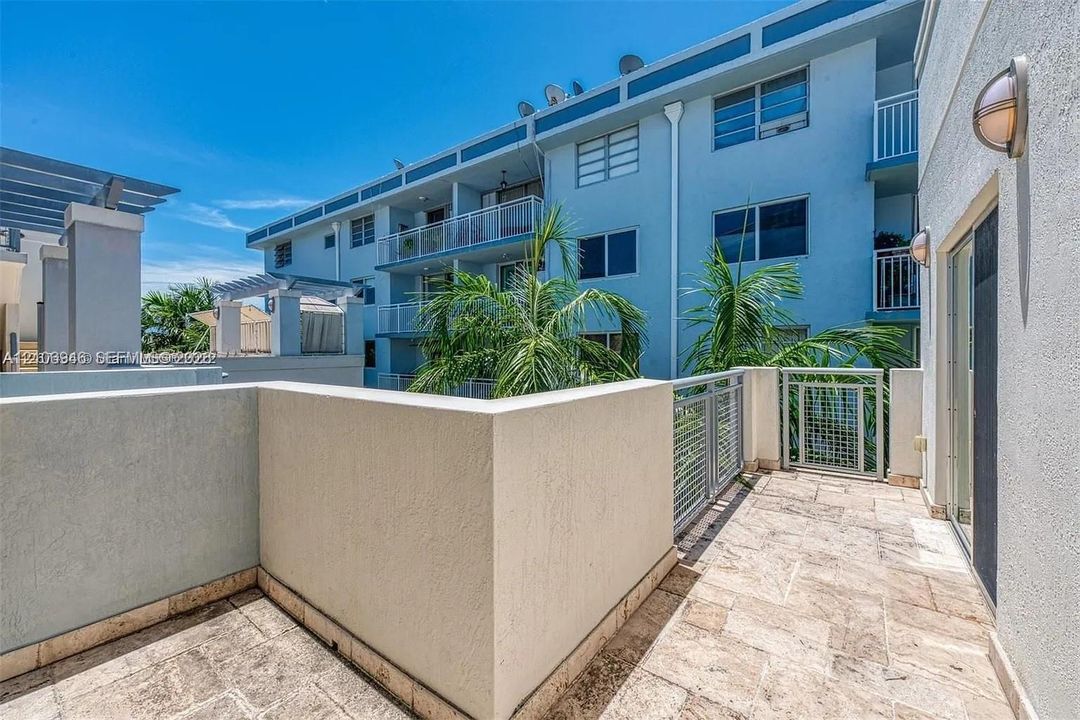 Private terrace featuring stone tile flooring, stucco privacy walls, metal railing, and wall-mounted exterior lighting