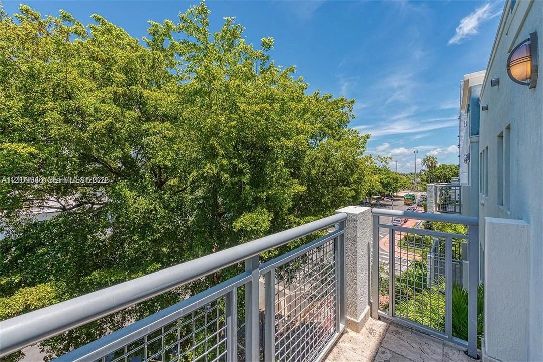 Exterior balcony featuring metal railings with grid-patterned panels, stone flooring, and wall-mounted exterior lighting
