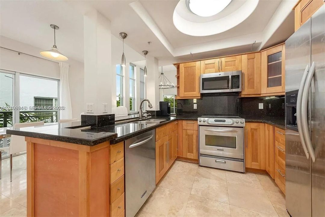 Kitchen featuring light wood cabinetry, dark stone countertops, stainless steel appliances, tile flooring, and a recessed ceiling with a circular skylight