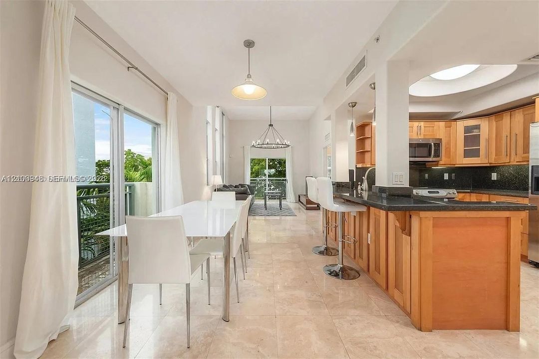 Kitchen featuring light-finish cabinetry, dark stone countertops, stainless steel appliances, breakfast bar, and stone flooring