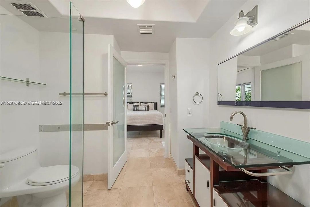 Bathroom featuring stone tile flooring, a glass-topped vanity with an integrated basin, a walk-in glass shower enclosure, and a modern wall-mounted mirror