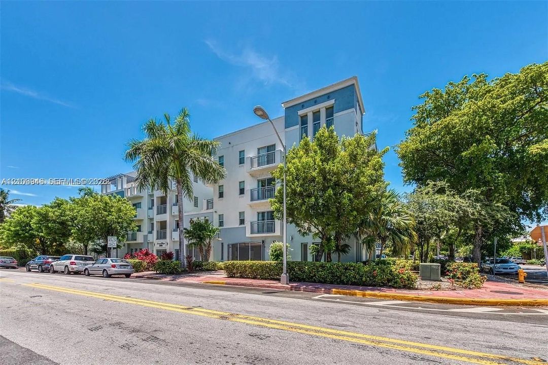 Multi-story residential building featuring a smooth stucco exterior, private recessed balconies, and mature palm and shade trees