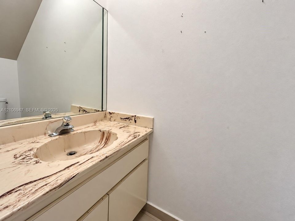 Vanity featuring a solid-surface countertop with an integrated basin, single-handle metal faucet, and wall-mounted mirror