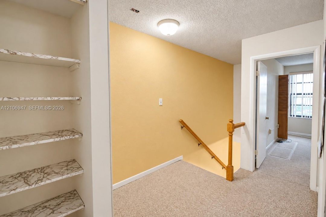 Built-in shelving with stone-finish surfaces, carpeted flooring, flush-mount ceiling lighting, and a staircase featuring a wooden handrail and baluster
