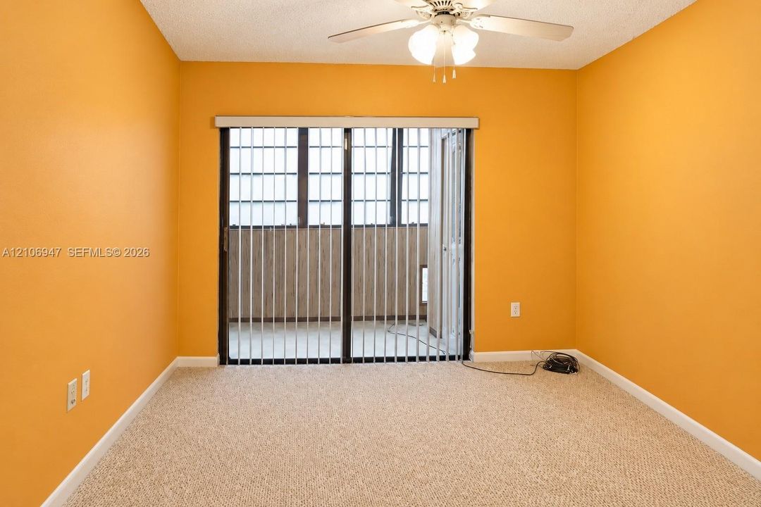 Interior space featuring wall-to-wall carpeting, a ceiling-mounted light fixture with fan, and a sliding glass door with vertical blinds