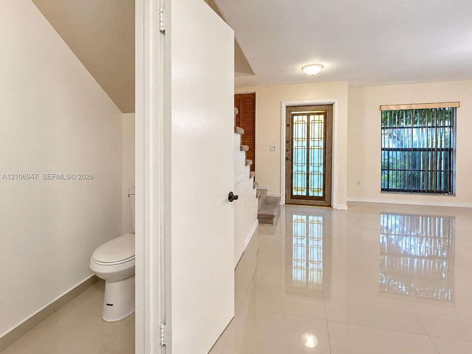 Polished tile flooring, entrance door featuring decorative glass inlay, window with vertical blinds, and stairs with carpeted treads
