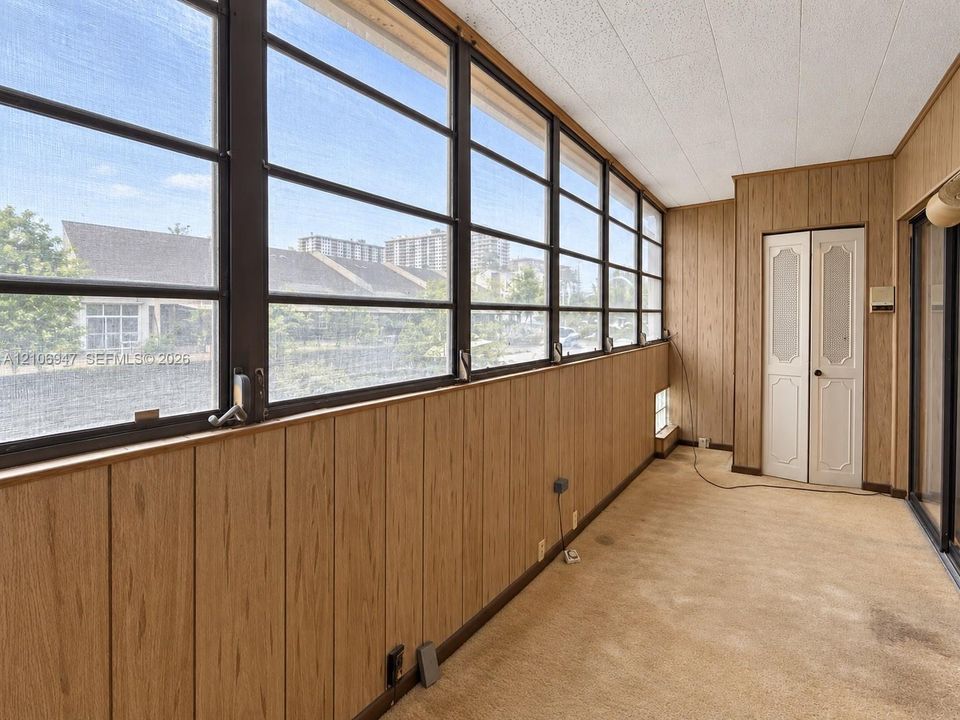 Enclosed space featuring vertical wood-finish wall paneling, a wall of multi-pane windows with metal framing, textured ceiling tiles, and dual-panel closet doors