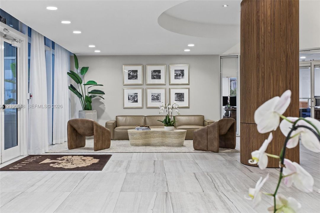 Large-format stone tile flooring, cylindrical wood-paneled structural column, recessed ceiling lighting, and floor-to-ceiling glass panel door