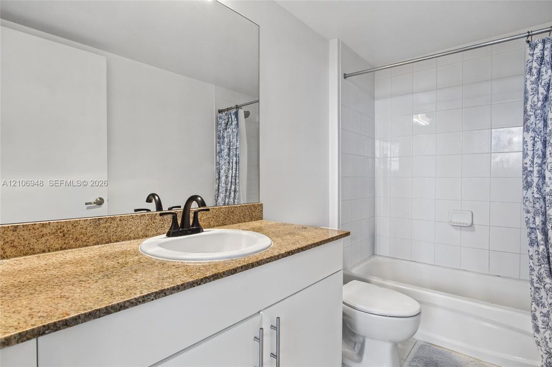Bathroom featuring a vanity with a stone-finish countertop, undermount sink, dark-finish hardware, full-width mirror, and a tub-shower combination with white wall tile