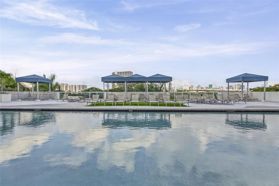 Rooftop swimming pool featuring a concrete deck, glass panel railings, and multiple shaded cabanas