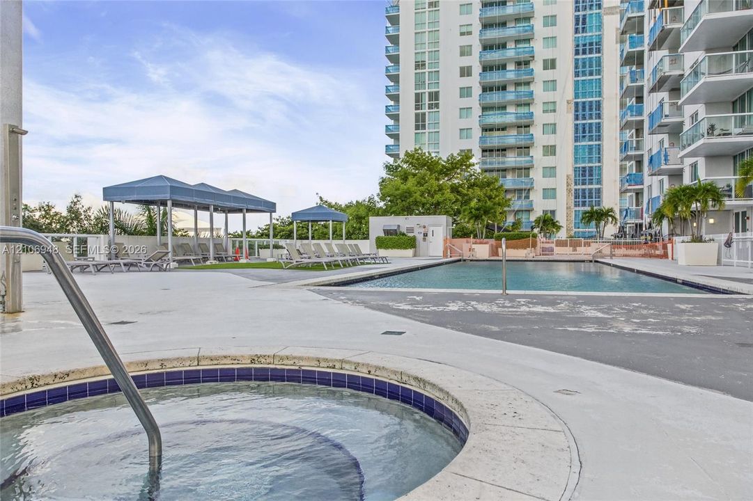 Outdoor terrace featuring a swimming pool, a circular spa with tile detailing, covered lounging structures, and paved decking