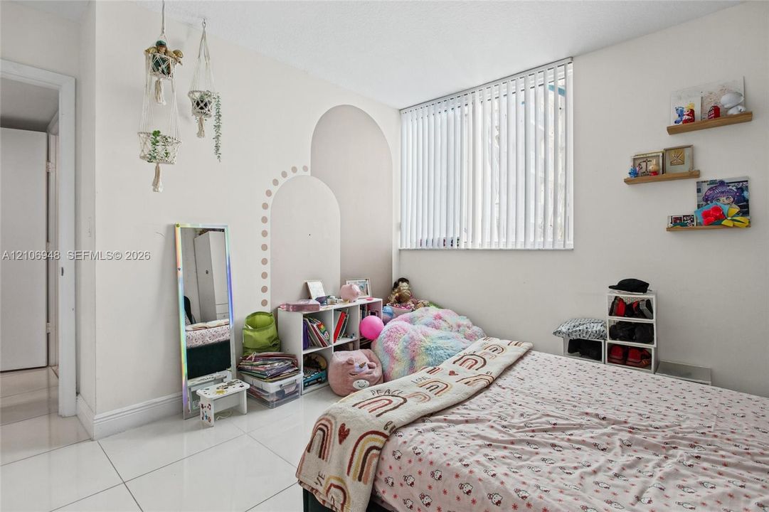 Room interior featuring smooth white flooring, decorative wall arches, vertical slat blinds, and wall-mounted shelving