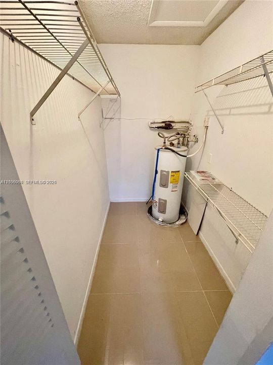 Utility closet featuring tile flooring, metal wall-mounted shelving, and an electric water heater