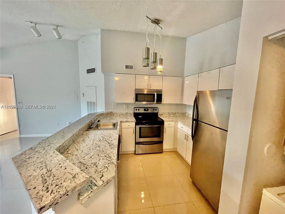 Kitchen featuring a raised breakfast bar with stone-finish countertops, white cabinetry, stainless steel appliances, and multi-light pendant illumination