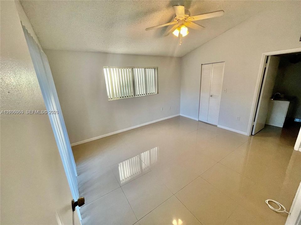 Vaulted ceiling, neutral large-format tile flooring, ceiling fan with integrated lighting, and built-in closet with double-panel doors