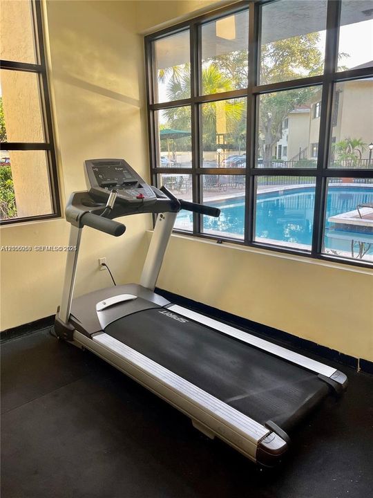 Floor-to-ceiling windows with dark framing, rubberized fitness flooring, and exterior exposure to a swimming pool