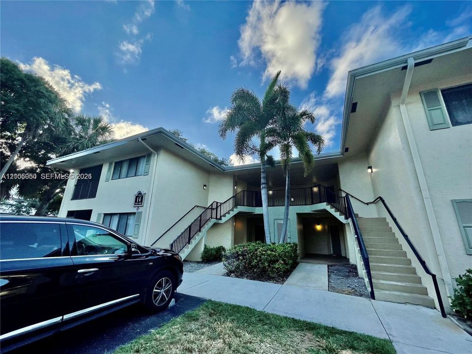Two-story exterior featuring light-colored stucco siding, black metal railings, concrete stairways, and mature landscaping