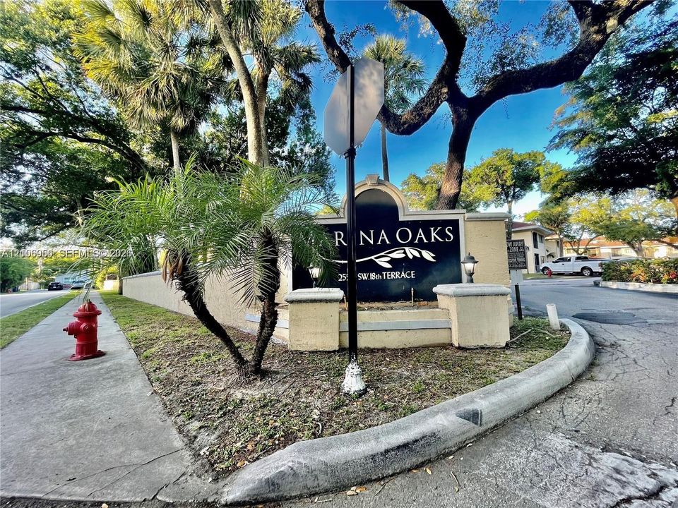 Entrance signage featuring a masonry monument with integrated lighting, framed by mature oak trees and palm landscaping