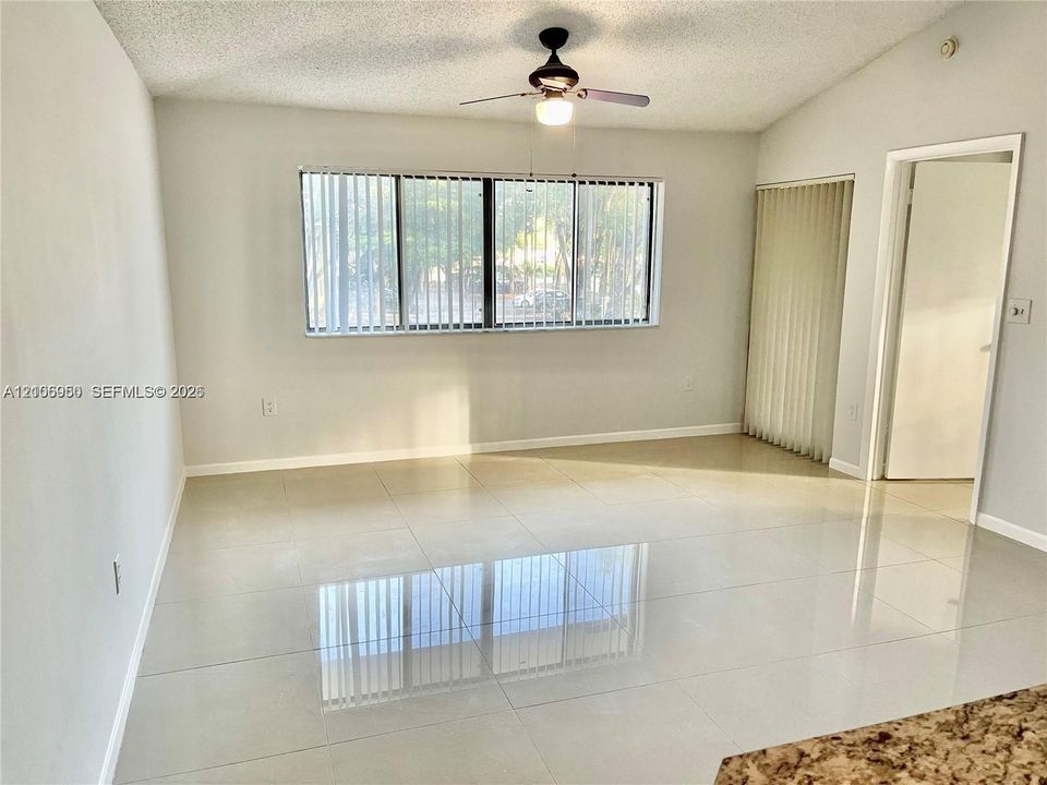Living space featuring large-format tile flooring, multi-pane window, ceiling fan with integrated light fixture, and vertical window blinds