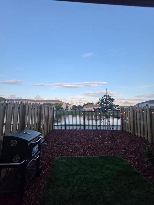Private backyard featuring a wood-style privacy fence, mulch landscaping, a small grass area, and a metal perimeter fence overlooking the water
