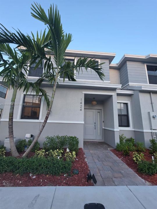Two-story exterior featuring a gray stucco and horizontal siding facade, paver walkway, recessed entryway, and mature palm trees