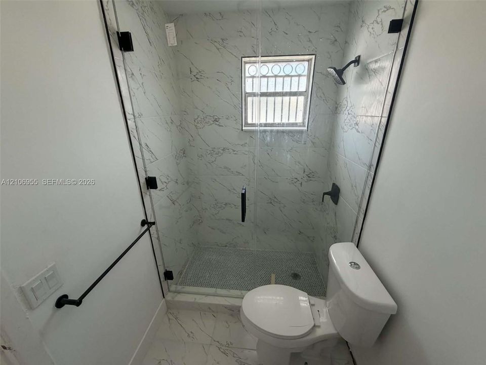 Walk-in shower featuring glass enclosure, stone-finish wall tile, penny tile flooring, and matte black hardware