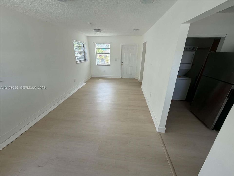 Interior space featuring light wood-finish flooring, neutral wall tones, multi-pane windows, and a dedicated laundry area with stacked appliances