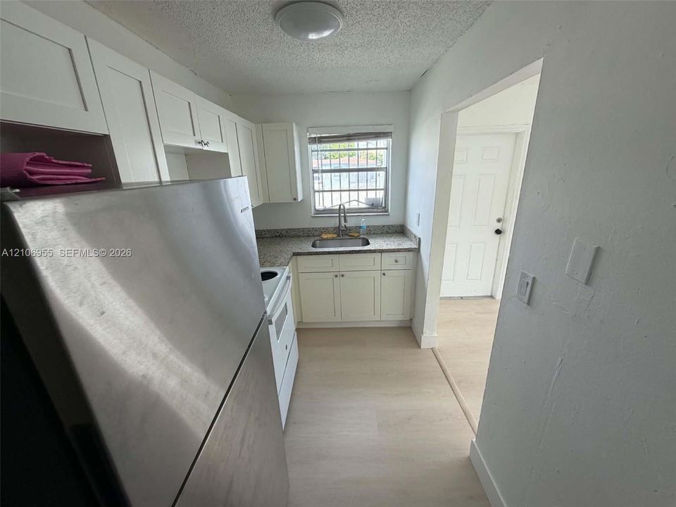 Kitchen featuring white cabinetry, stone-finish countertops, stainless steel refrigerator, and wood-finish flooring
