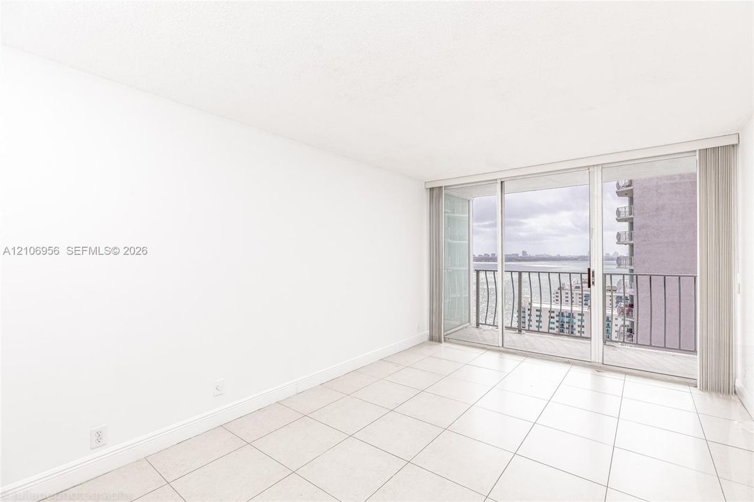 Neutral tile flooring, floor-to-ceiling glass sliding doors, and a private balcony featuring metal railings