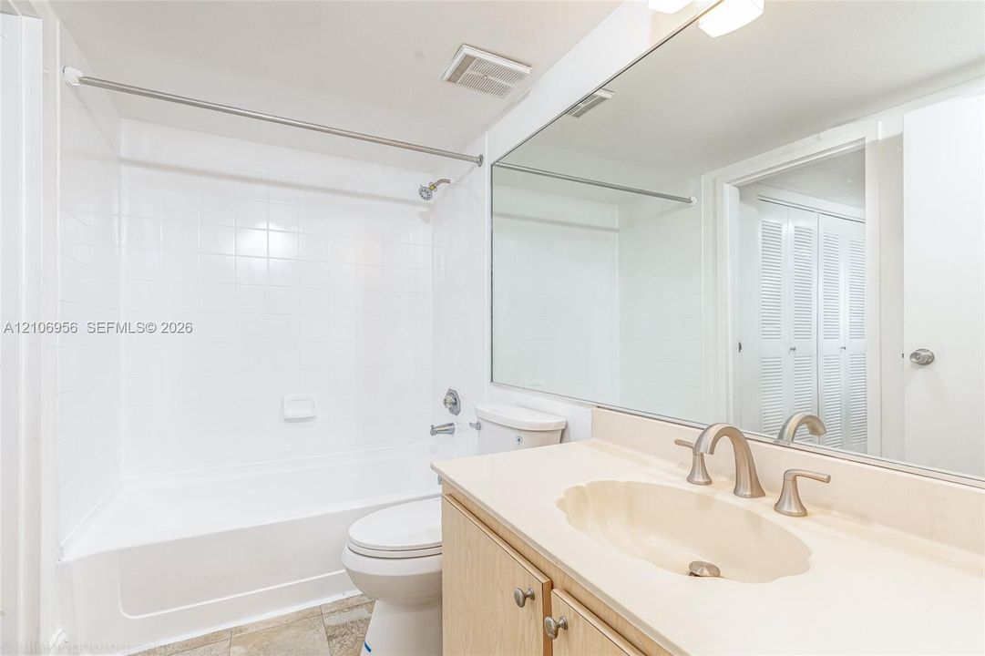 Bathroom featuring a shower and tub combination with a tiled surround, a large wall-mounted mirror, a vanity with a molded countertop, and louvered closet doors