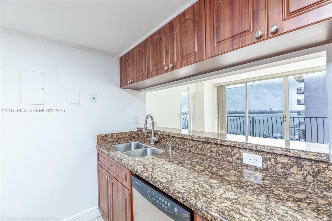 Kitchen featuring wood-tone cabinetry, stone-patterned countertops, a dual-basin stainless steel sink with a high-arch faucet, and an integrated dishwasher