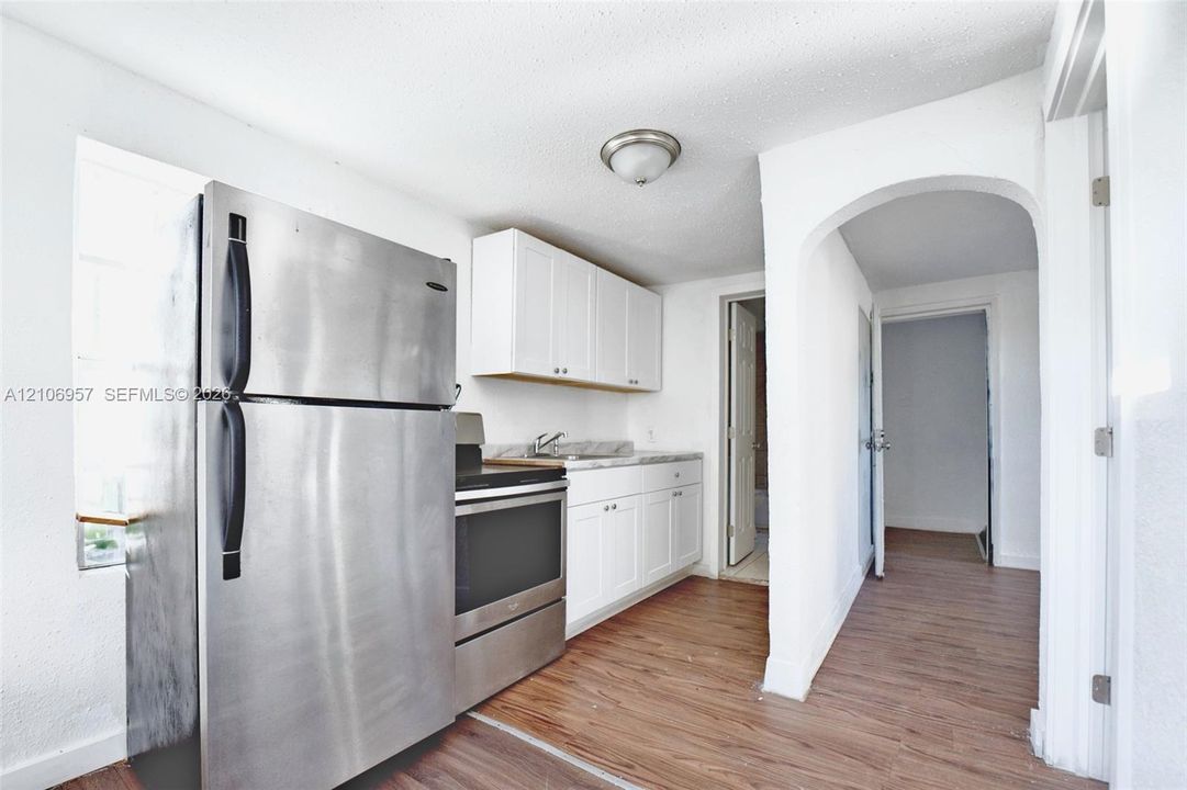 Kitchen featuring stainless steel refrigerator and range, white cabinetry, solid-surface countertops, and wood-finish flooring