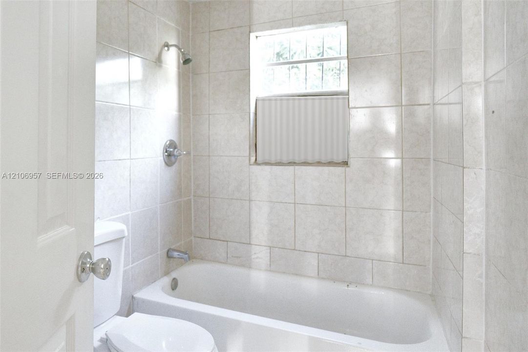Tiled bath with tub and shower. Virtually staged: window treatment added digitally.